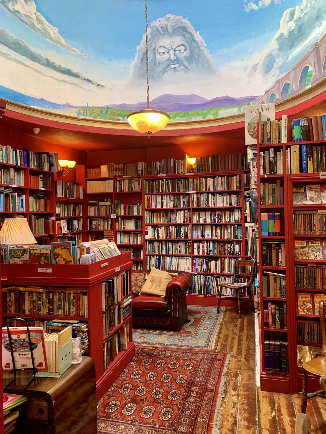 Inside Slightly Foxed: red shelving floor to ceiling, a leather reading chair on a Persian rug, and the famous hand-painted dome ceiling above